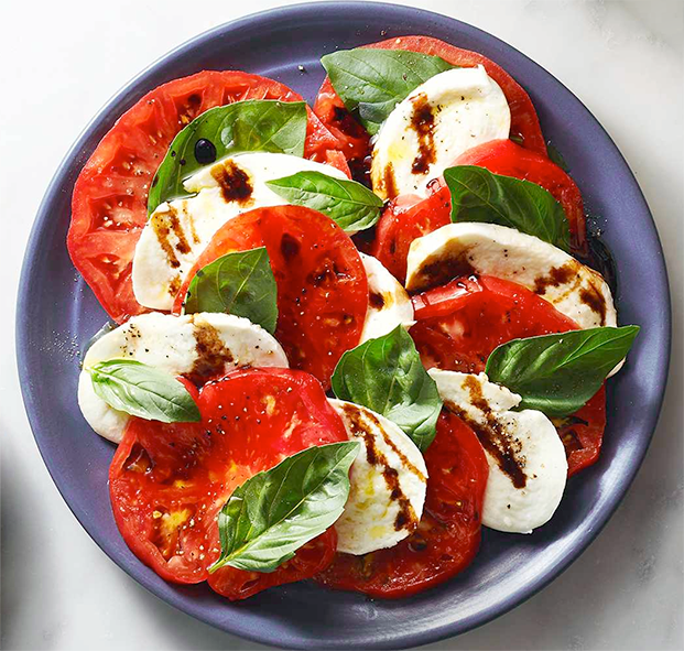 Caprese salad of tomatoes, mozzarella and basil leaves served overlapping on a purple plate