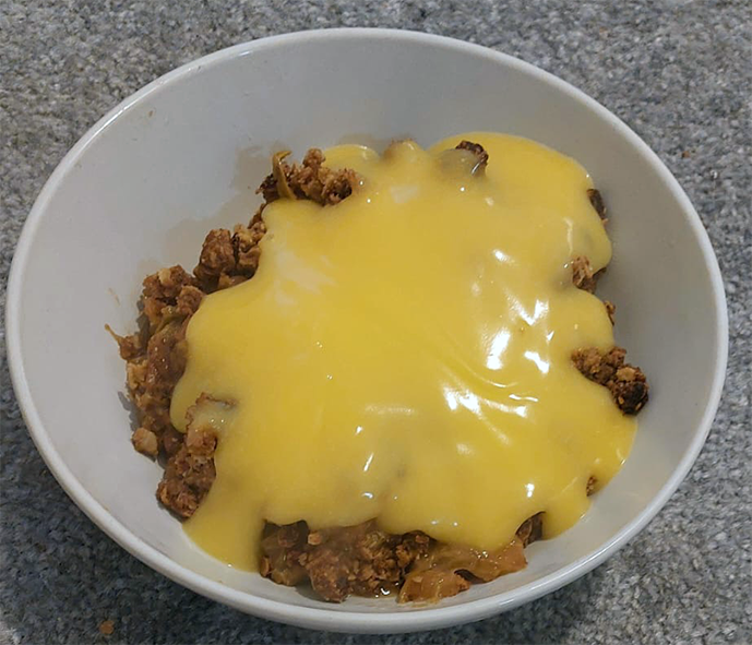 Japanese knotweed crumble served topped with custard in a white bowl