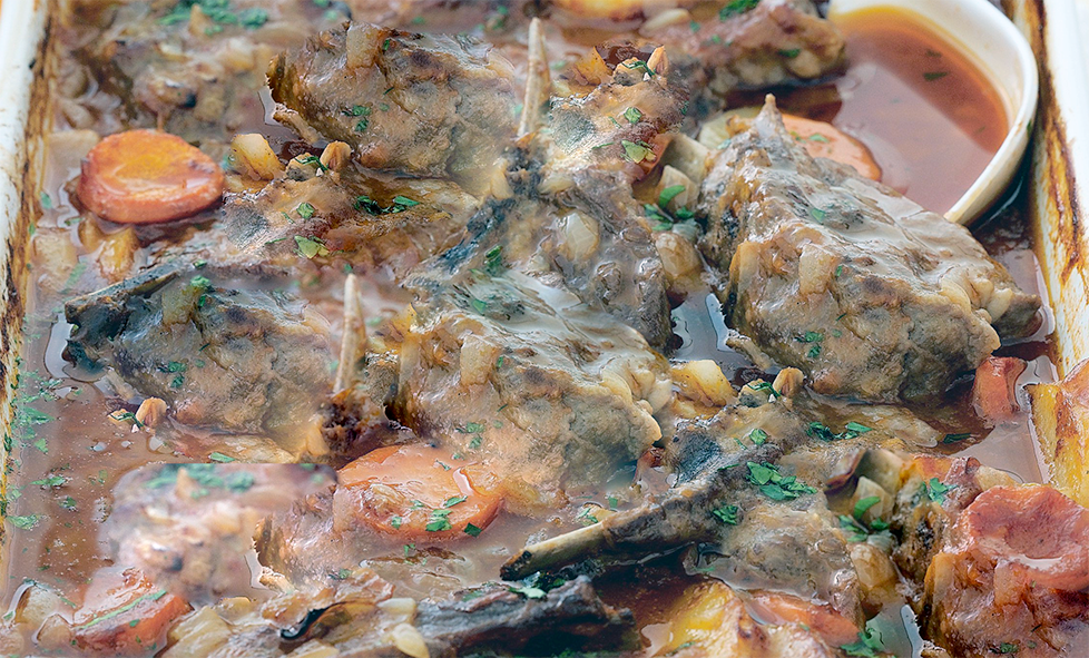 lamb cutlet casserole with carrots in a white baking dish with a spoon