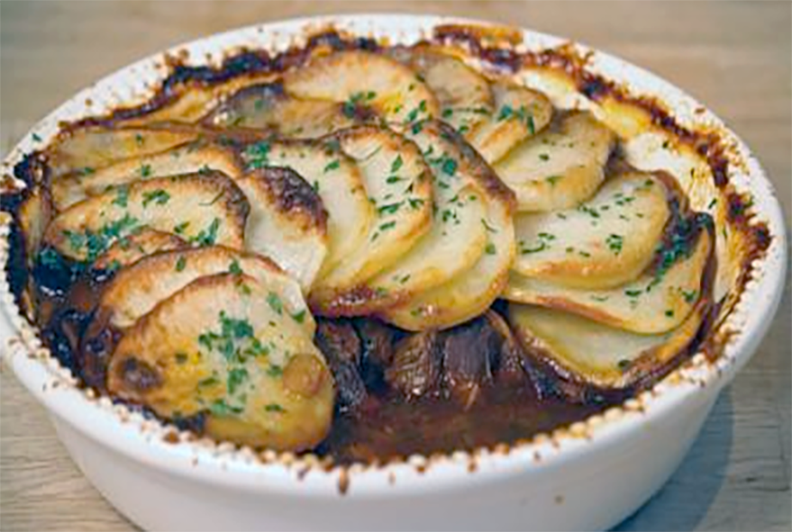 lancashire hotpot in a white baking dish with some of the potato topping removed to reveal the filling
