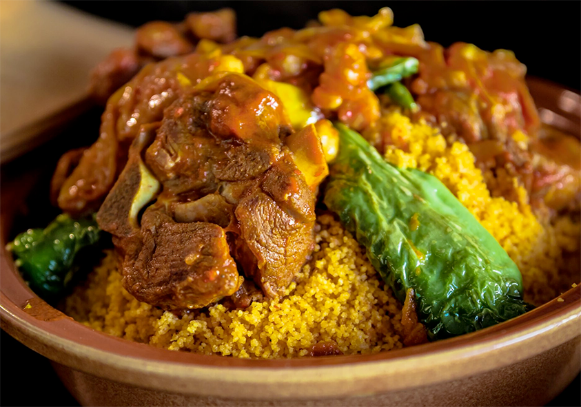 an earthenware dish piled with couscous which is topped with lamb pieces and vegetables