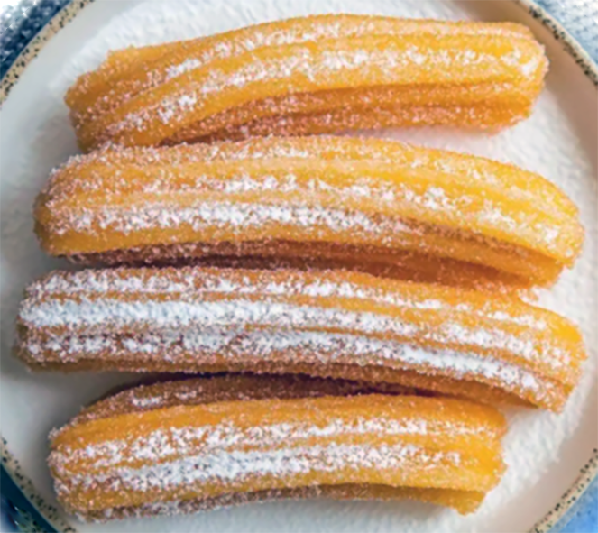 four Mexican churros arranged on a plate and dusted with powdered sugar
