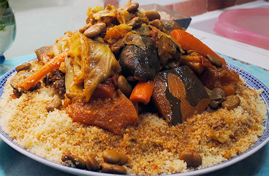 a plate piled with couscous which is topped with lamb pieces and vegetables