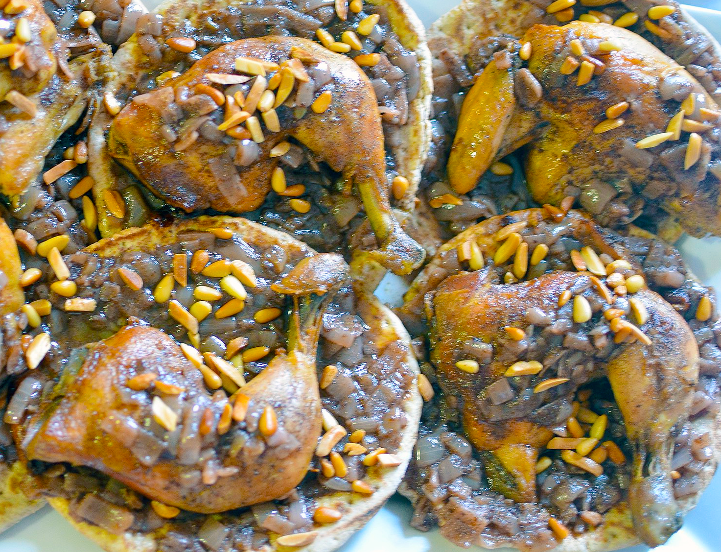 baked chicken with onions served on individual flatbreads and garnished with pine kernels and almond slivers