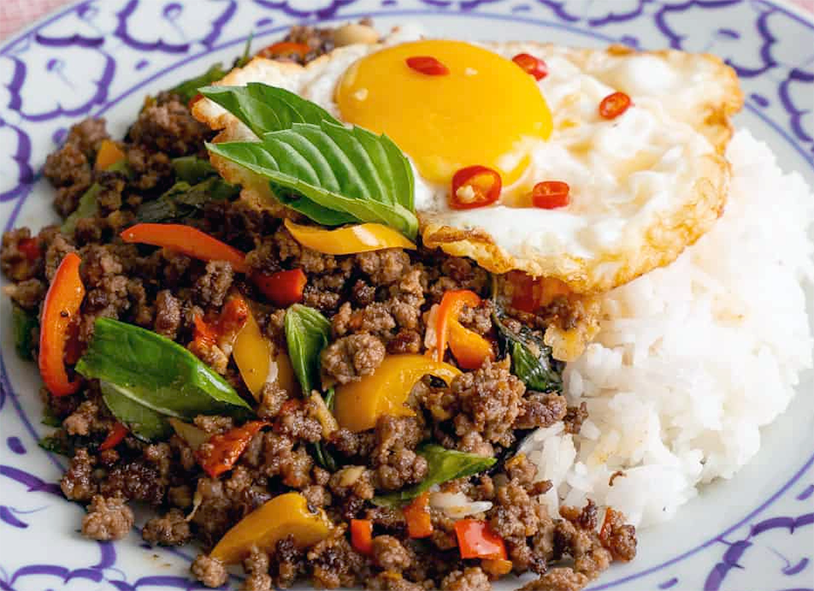pad kra pao stir-fry served with boiled jasmine rice and garnished with a fried egg, holy basil leaves and sliced chilli
