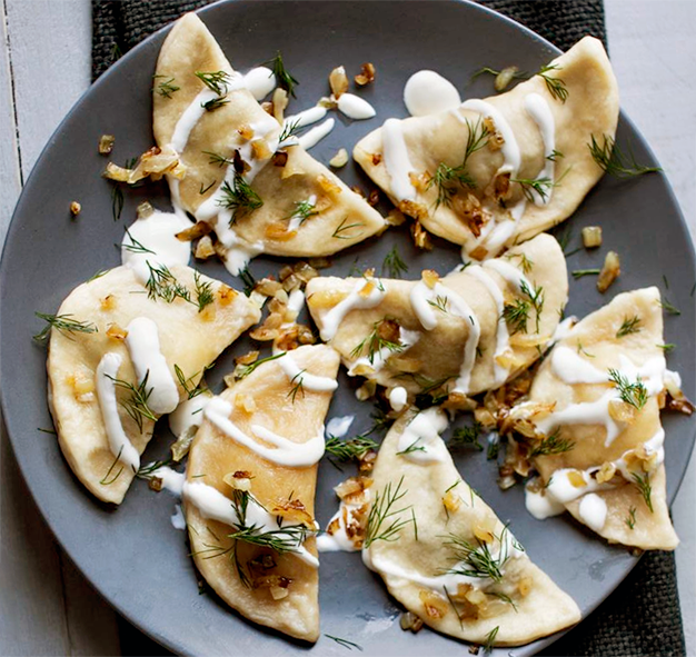 pieorogi dumpings arranged on a plate with a garnish of soured cream and dill