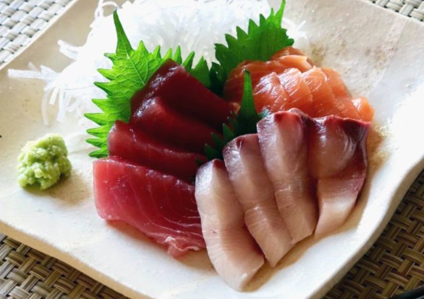three fish sashimi served on a plate with wasabi, shiso leaves and grated daikon