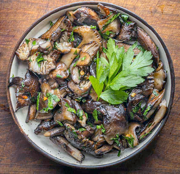 sauteed honey fungus caps and stems arranged on a plate and garnished with a lovage leaf