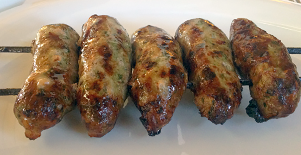 five seftali kebabs threaded on two skewers and served on a white plate