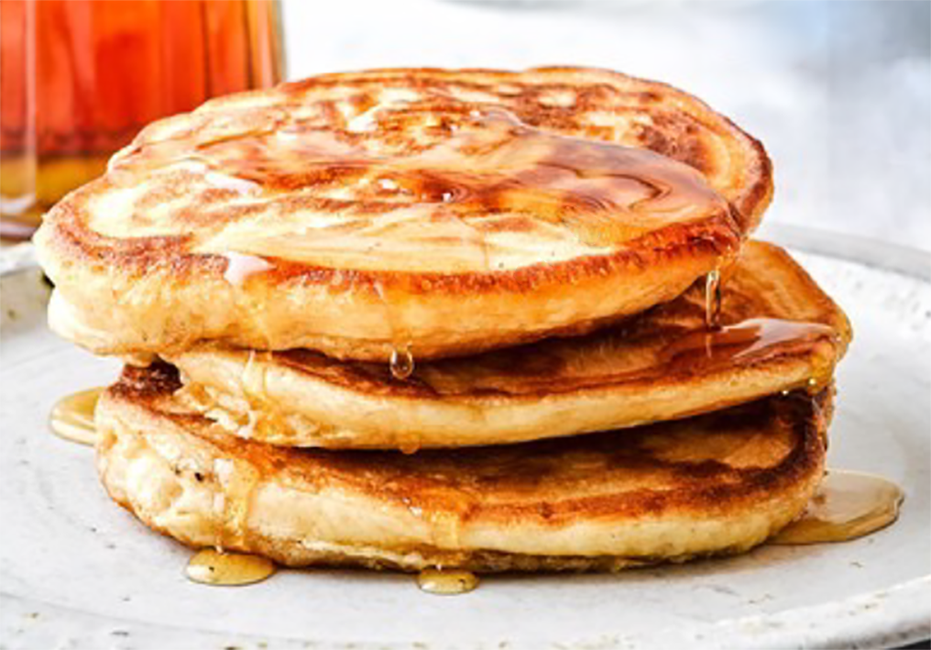 three sourdough pancakes piled on a plate and drizzled with maple syrup