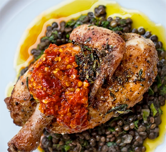 half a spatchcocked poussin served on a bed of lentils and topped with harissa