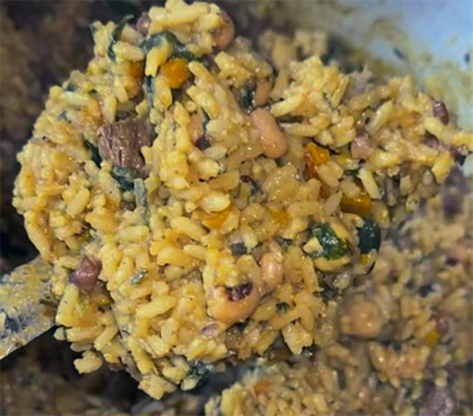 one-pot dish of saffron rice, beans and smoked meat held on a spoon