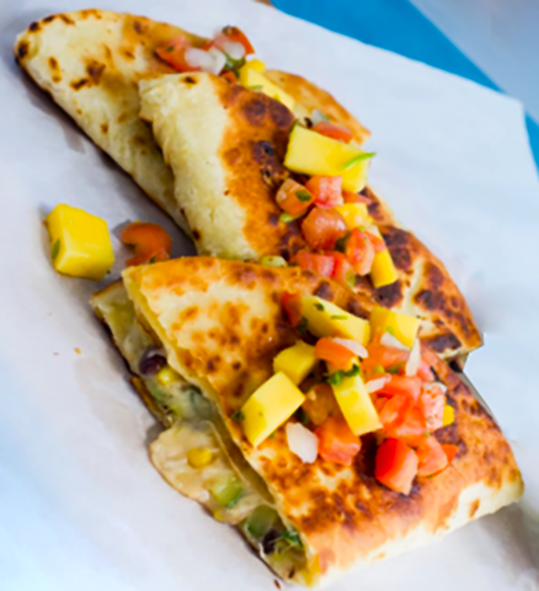 mexican quesadilla on a sheet of greaseproof paper served topped with tomato and avocado