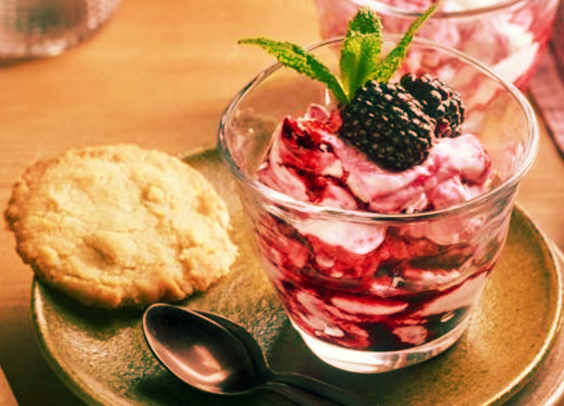 blackberry fool served in a glass topped with blackberries and a sprig of mint served with a hazelnut biscuit