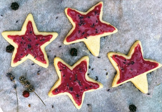four blackberry iced star biscuits on a sheet of greaseproof paper with blackberries