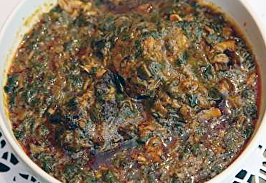 alt stew of beef, fish and cassava leaves in a peanut and red oil base served in a bowl
