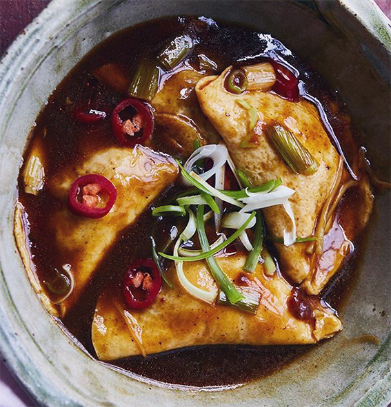 three egg dumplings in a dark chilli broth in a green-glazed bowl
