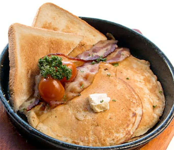 breakfast pancakes in a skillet with bacon, fried tomatoes and toast