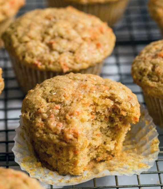 carrot muffins on a wire rack with a bite taken out of one to reveal the centre