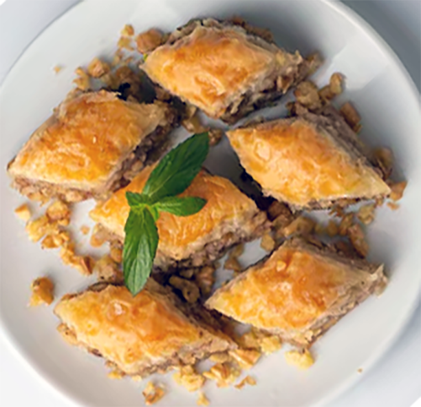 diamonds of walnut (cevizli) baklava arranged on a white plate garnished with a sprig of mint