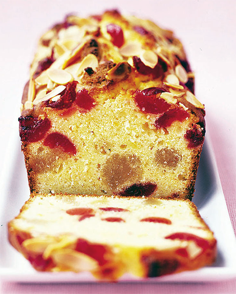 cherry and almond loaf cake on a serving plate with one slice cut to reveal the centre