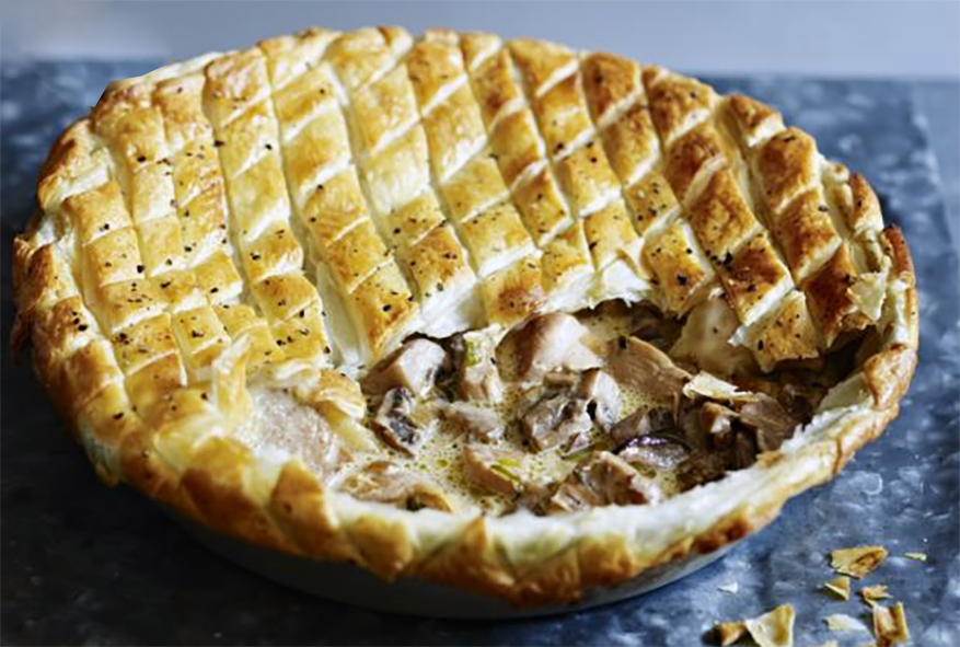 Chicken and mushroom pot pie with a flaky pastry crust shown with a wedge removed to reveal the filling