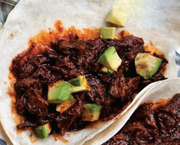 chilorio (Shredded Pork in Ancho-Orange Sauce) served on a tortilla with a garnish of diced avocado