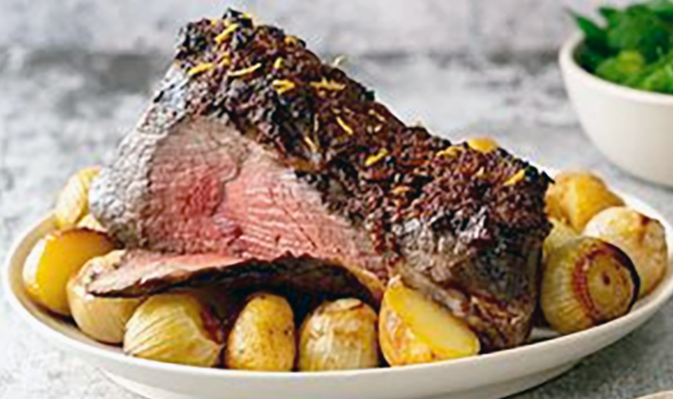 roast lamb with one slice partly cut served on a plate and surrounded by roast potatoes