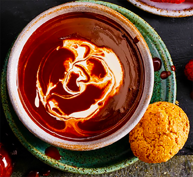 coffee liqueur fondue in a bowl with a garnish of cream and a biscuit on the side