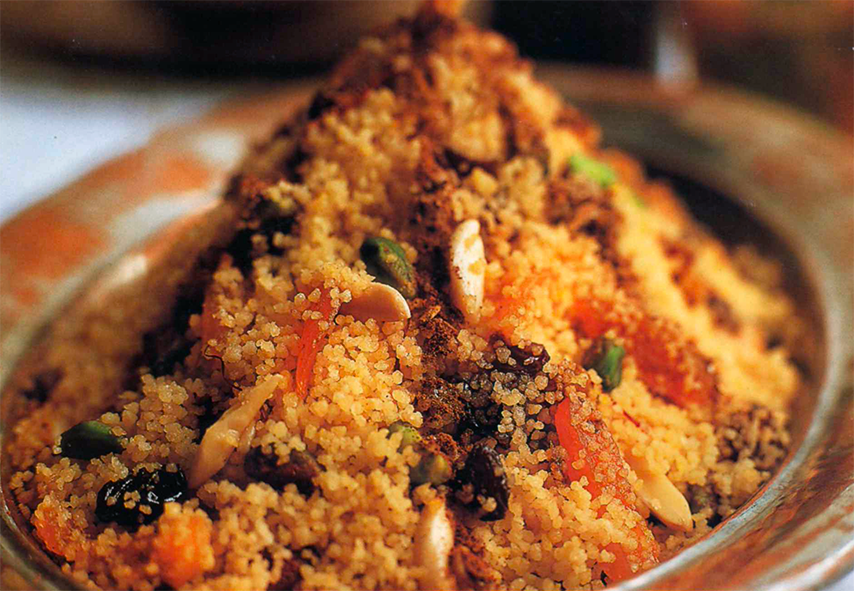 couscous with dried fruit and nuts shown mounded on a silver dish and garnished with rows of ground cinnamon and caster sugar
