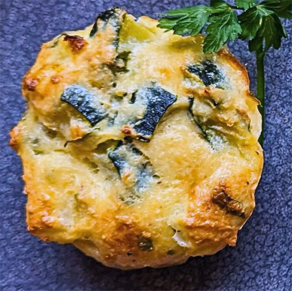 muffin with dill, courgette and ricotta on a blue plate with a sprig of flat-leaf parsley
