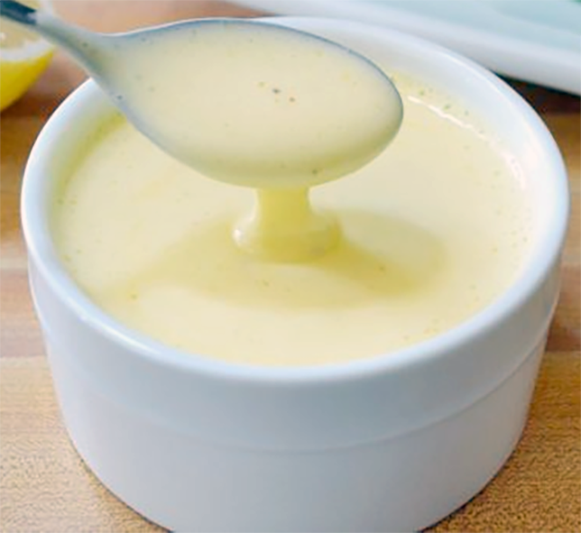 Dutch/Hollandaise sauce drizzled from a tablespoon into a white ramekin