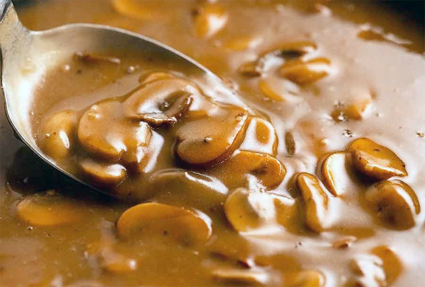 Spoon lifting some sliced mushrooms from the brown fine-herbs sauce