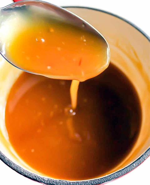 sweet orange sauce dripping from a spoon into a small saucepan
