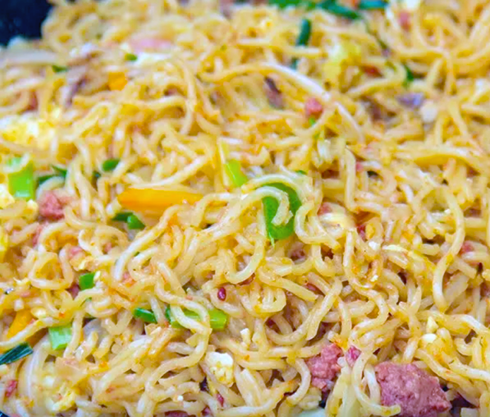 instant noodles (indomie) served with frankfurter pieces, chilli, green bell pepper, cabbage and spring onions