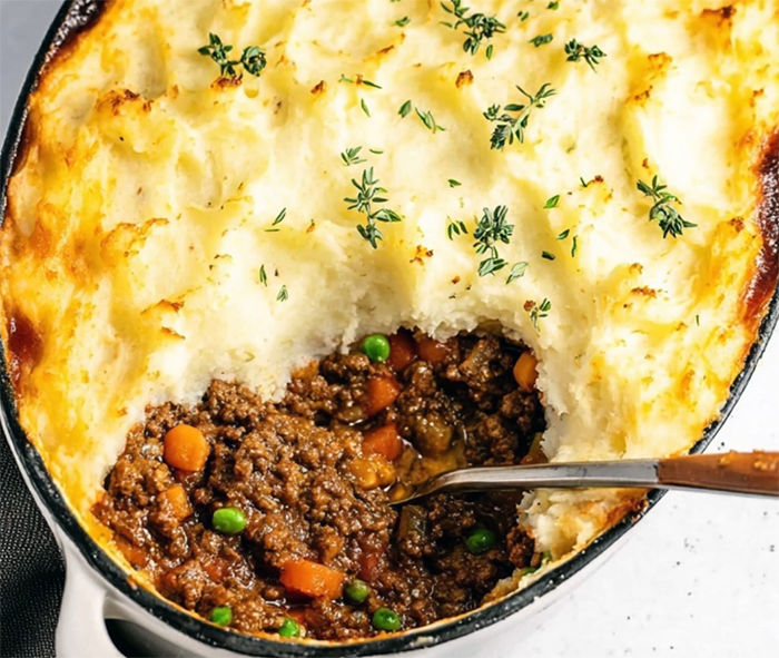 goatherd's pie with mashed potato topping in a baking dish with one section of the potatoes removed to reveal the filling