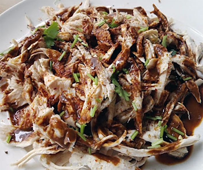 bang-bang chicken — shredded chicken served on a white plate topped with a spicy sauce
