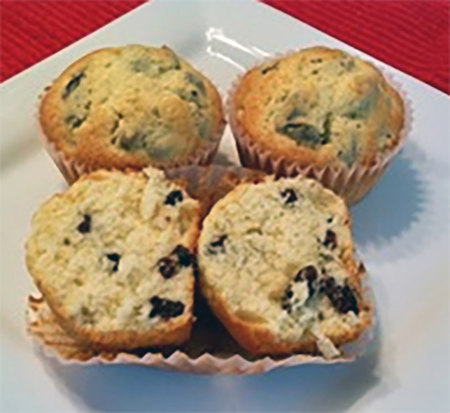 three heirloom raisin muffins in paper cases on a plate with one split to reveal the centre