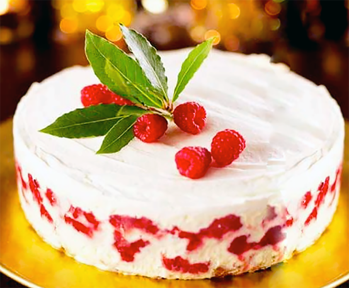 whole iced raspberry and eggnog trifle cake garnished with raspberries and a sprig of bayleaves on a golden plate