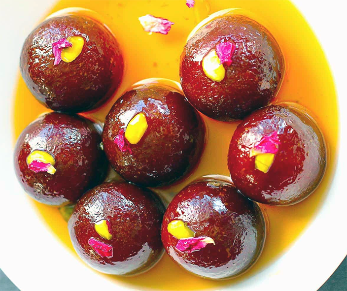 gulab jamun balls served in a white bowl with syrup