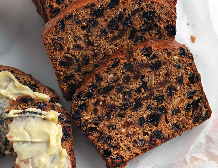 slices of fruited treacle loaf on a chopping board with one slice buttered