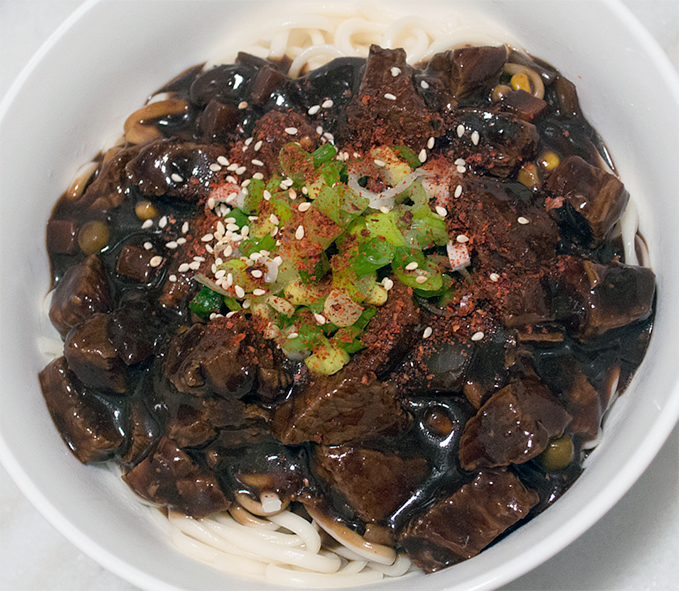 jajangmyeon noodles topped with pork in black bean sauce and a fresh garnish
