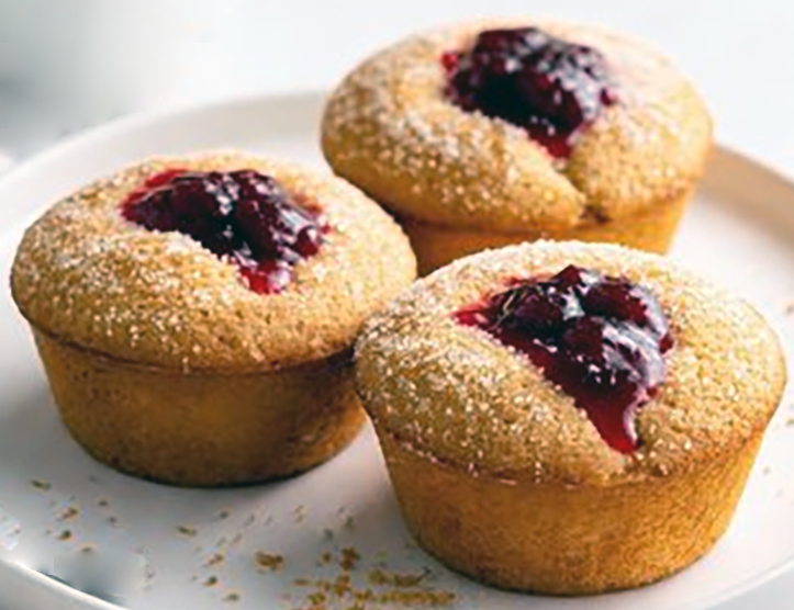 three cornmeal muffins with jam baked into their tops arranged on a plate