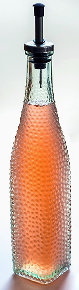 pink Japanese knotweed syrup in a tall frosted glass bottle