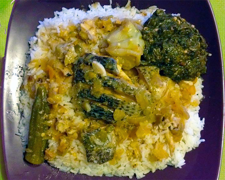 whole fish in a red oil sauce served on a bed of rice with okra, bitterball and hibiscus leaf paste garnish