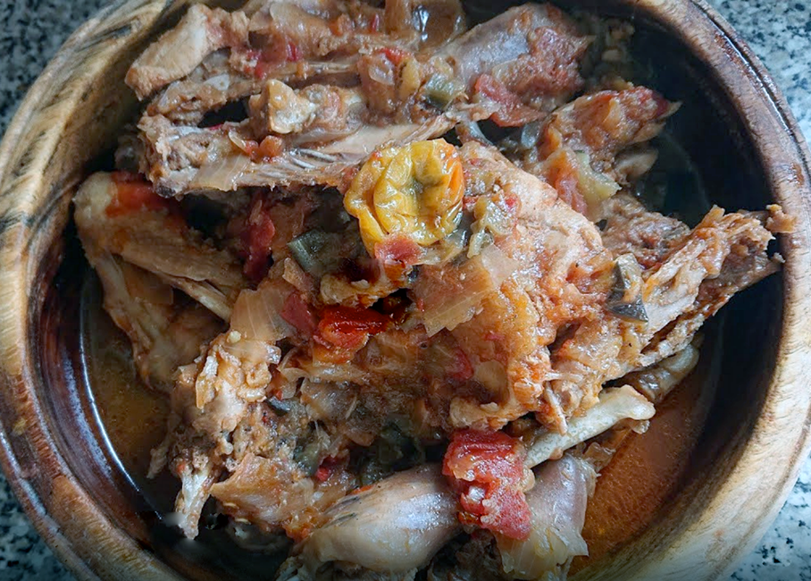 Kedjenou guinea fowl stew with tomatoes shown topped with a yellow chilli in an earthenware bowl