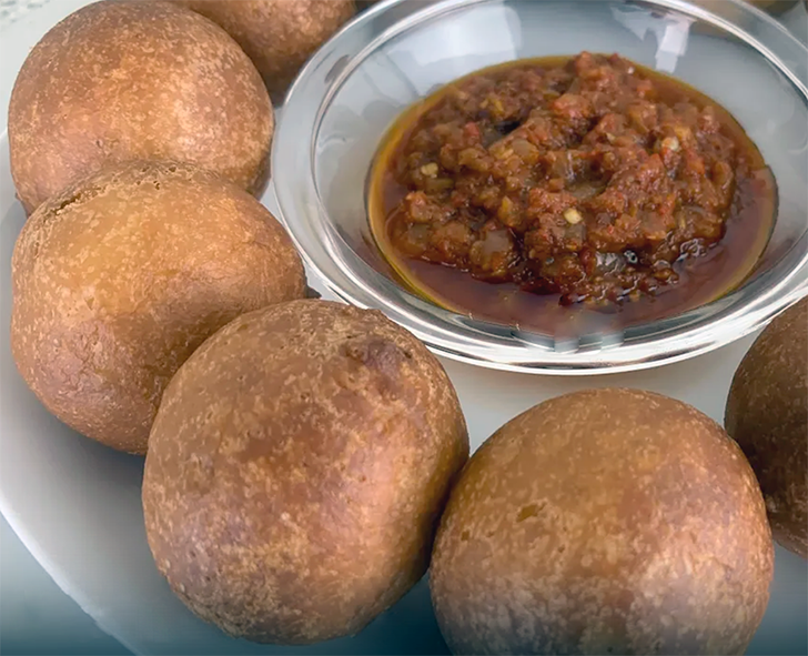 balls of sweetened yeasted flour dough surrounding and served with a pepper sauce