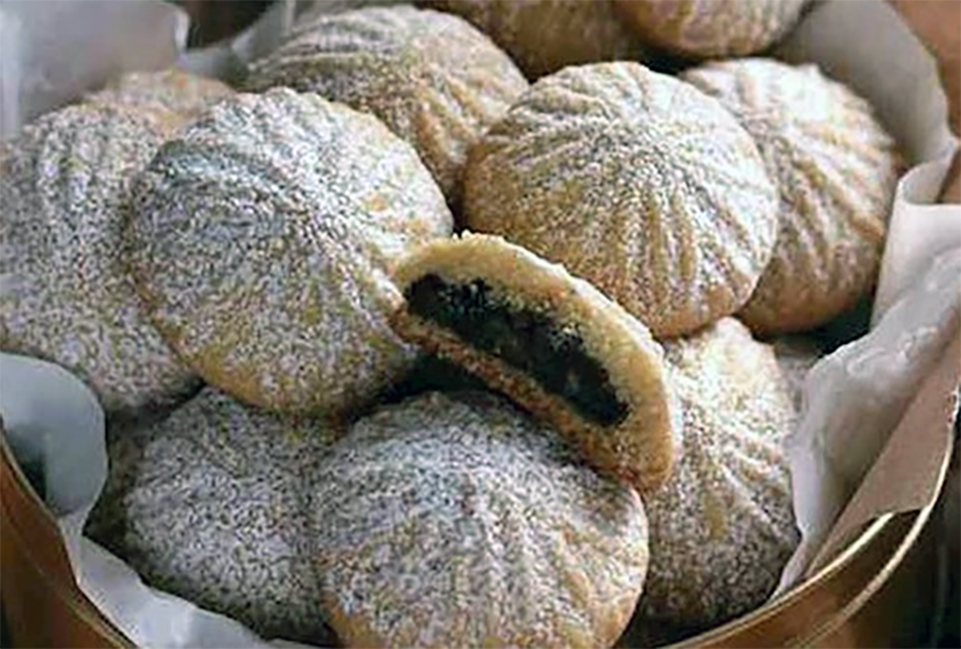 Ma'amool B'jowz biscuits in a tin with one split in half to reveal the filling