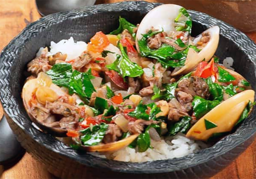 Sao Tomean clam, pumpkin and peanut stew with greens served in a bowl on a bed of rice