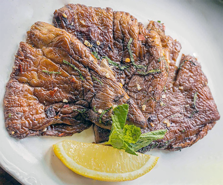 fried shaggy parasol mushrooms arranged in a fan on a plate with a sprig of mint and a wedge of lemon